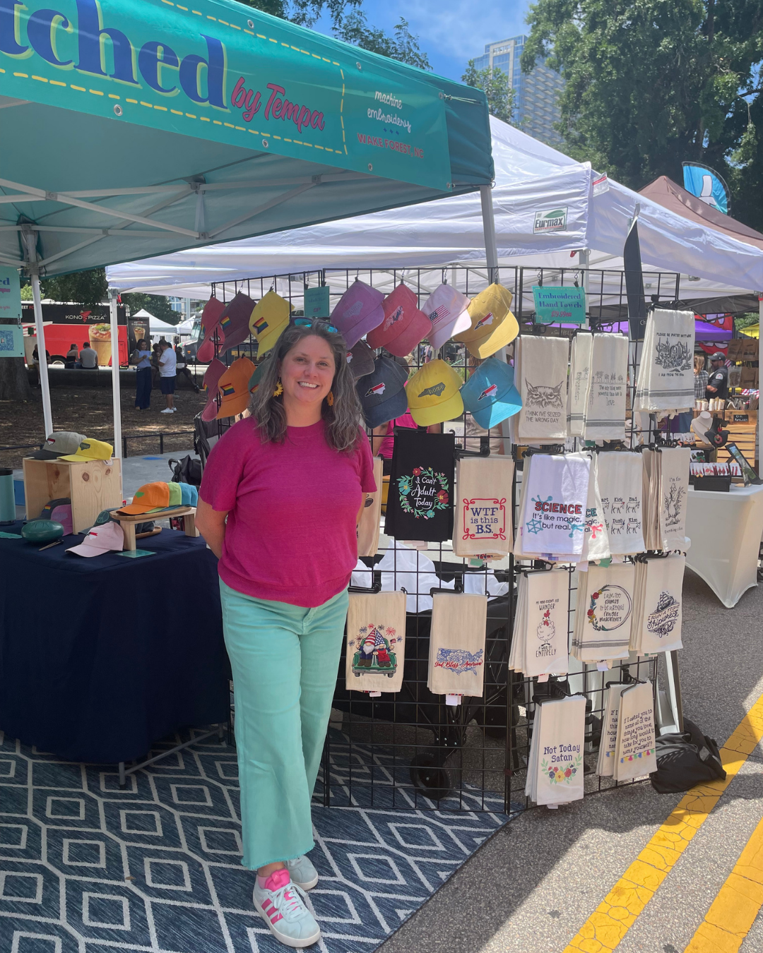 Tempa from Stitched by Tempa at a craft market booth in Raleigh, NC, displaying embroidered towels and hats