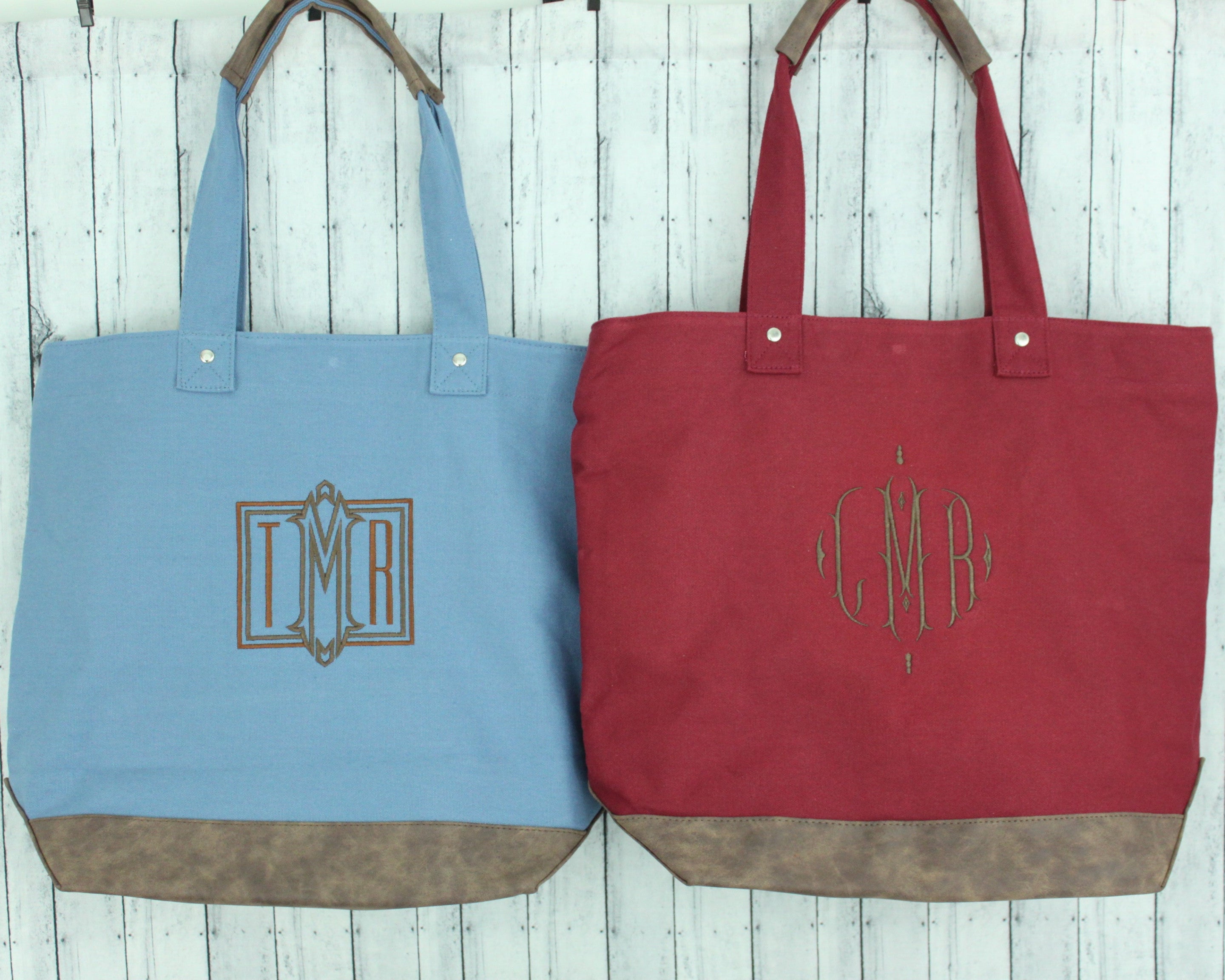 Two tote bags, one blue and one red, with monogrammed initials on a wooden surface.